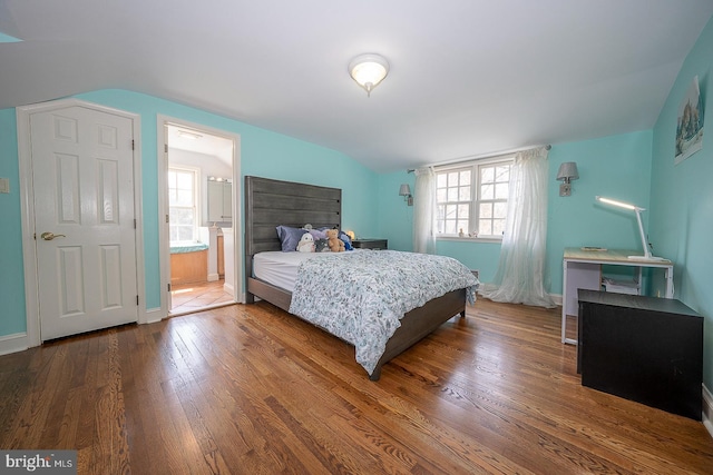 bedroom with ensuite bath, hardwood / wood-style flooring, vaulted ceiling, and multiple windows