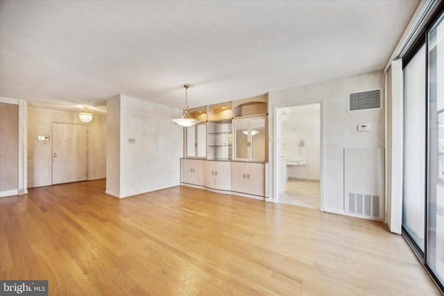 unfurnished living room with plenty of natural light, light hardwood / wood-style floors, and a textured ceiling