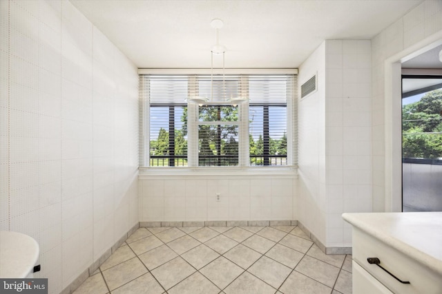 unfurnished dining area featuring light tile patterned floors and tile walls