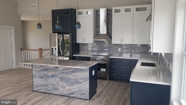 kitchen with white cabinetry, a center island, wall chimney exhaust hood, light hardwood / wood-style flooring, and appliances with stainless steel finishes