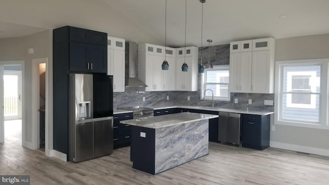 kitchen with a center island, white cabinets, wall chimney range hood, sink, and stainless steel appliances