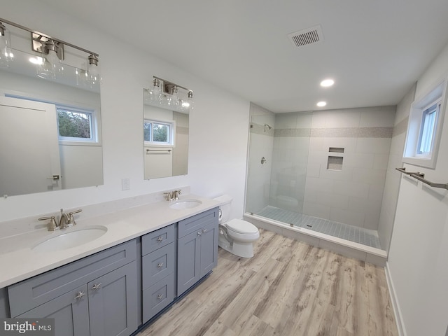 bathroom featuring a tile shower, vanity, wood-type flooring, and toilet