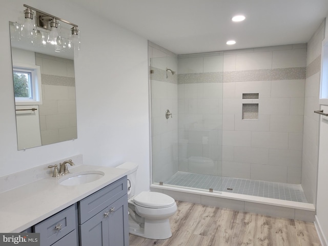 bathroom with tiled shower, wood-type flooring, vanity, and toilet