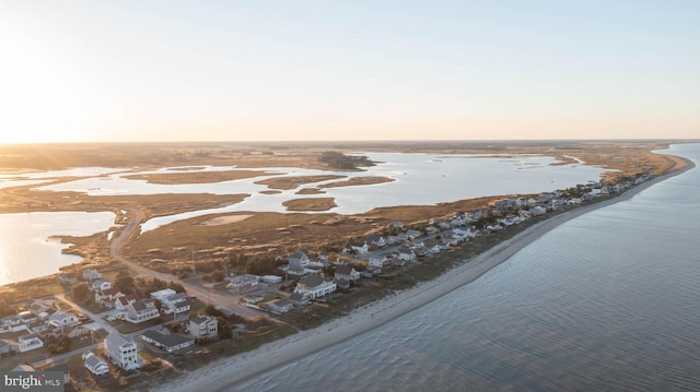 aerial view at dusk featuring a water view and a beach view