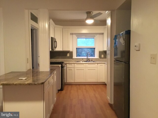 kitchen with stainless steel appliances, sink, light hardwood / wood-style floors, white cabinetry, and ceiling fan