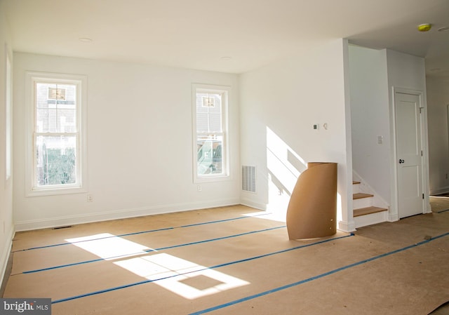 unfurnished living room featuring stairs, visible vents, and baseboards