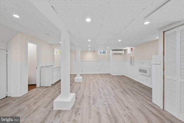 basement featuring a drop ceiling, light wood-type flooring, and a wall unit AC