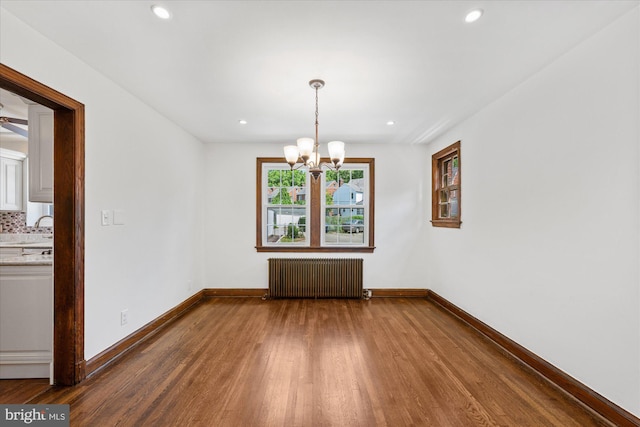 unfurnished dining area with hardwood / wood-style floors, radiator heating unit, and a chandelier