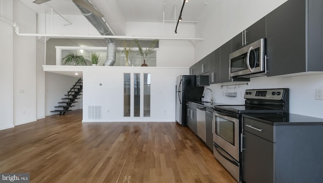 kitchen featuring a towering ceiling, appliances with stainless steel finishes, light wood-type flooring, and sink