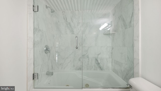 bathroom featuring toilet and shower / bath combination with glass door