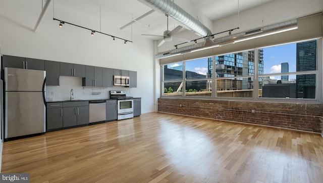 kitchen with a high ceiling, sink, ceiling fan, appliances with stainless steel finishes, and brick wall