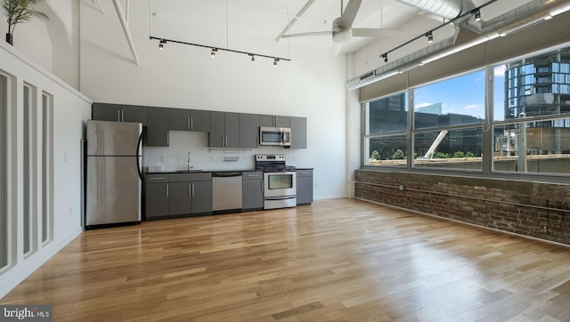 kitchen with a towering ceiling, stainless steel appliances, ceiling fan, and brick wall