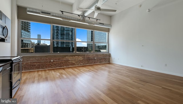 unfurnished living room featuring ceiling fan, a healthy amount of sunlight, light wood-type flooring, and a towering ceiling