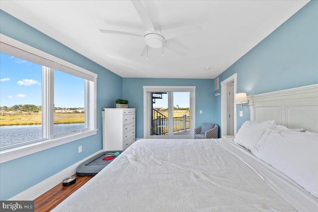 bedroom featuring access to exterior, ceiling fan, a water view, and hardwood / wood-style flooring