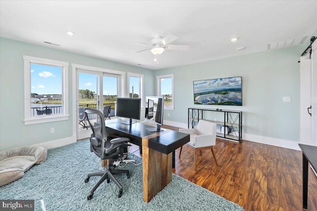 office space featuring a barn door, a wealth of natural light, dark wood-type flooring, and ceiling fan