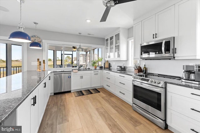 kitchen featuring appliances with stainless steel finishes, light wood-type flooring, dark stone counters, white cabinets, and hanging light fixtures