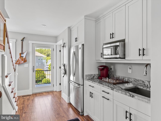 kitchen with dark wood-type flooring, sink, appliances with stainless steel finishes, light stone counters, and white cabinetry