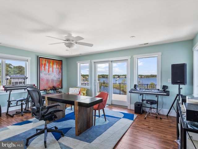 home office with ceiling fan, a water view, and wood-type flooring