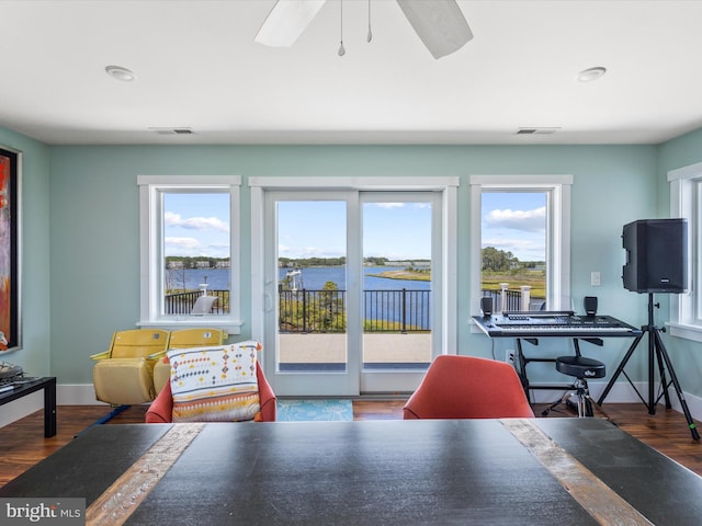 dining room with dark hardwood / wood-style flooring, a healthy amount of sunlight, a water view, and ceiling fan