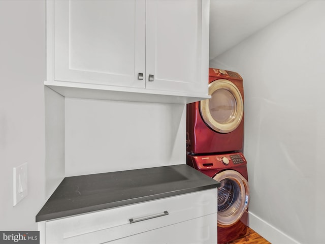 clothes washing area with cabinets, stacked washer / drying machine, and hardwood / wood-style flooring