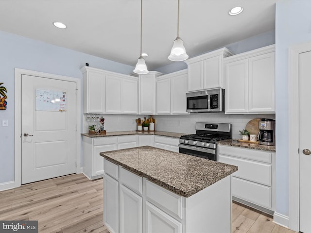 kitchen with appliances with stainless steel finishes, dark stone countertops, white cabinets, a center island, and hanging light fixtures