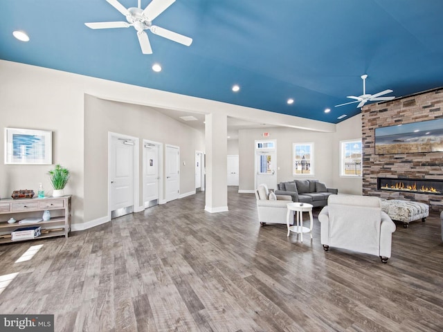 living room with hardwood / wood-style floors, vaulted ceiling, ceiling fan, and a stone fireplace