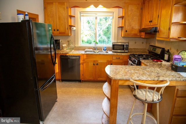 kitchen with kitchen peninsula, light stone countertops, sink, black appliances, and a breakfast bar area