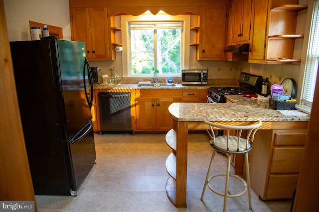 kitchen featuring sink, light stone counters, kitchen peninsula, a kitchen bar, and black appliances