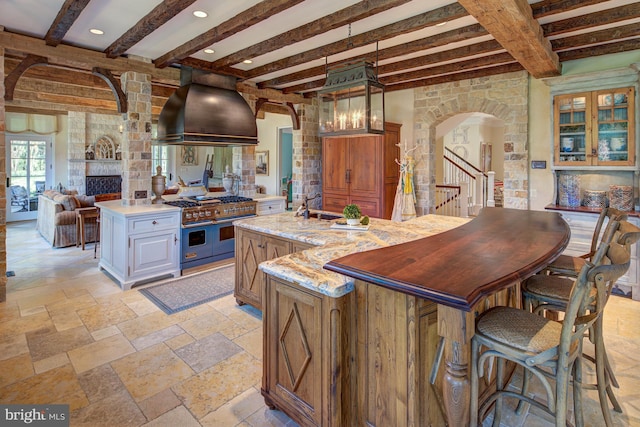 kitchen featuring beam ceiling, a kitchen island with sink, custom range hood, and range with two ovens