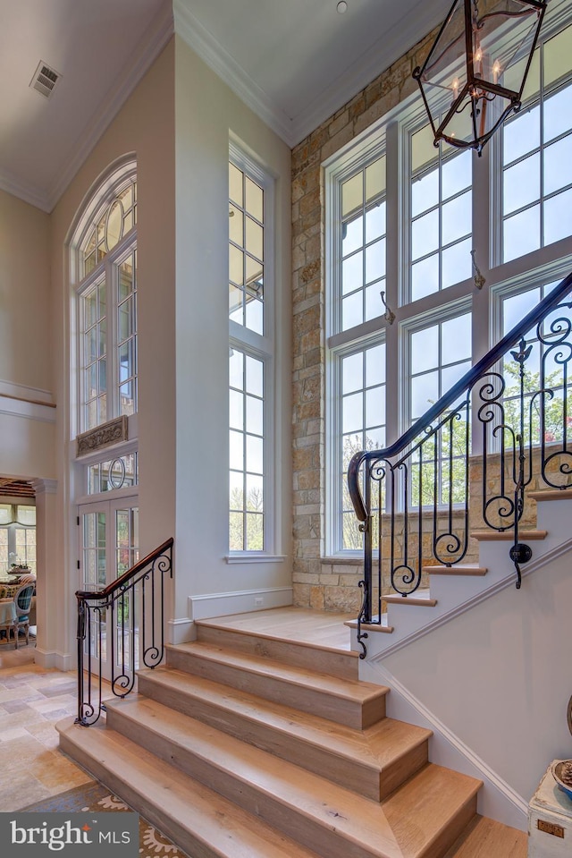 staircase featuring a notable chandelier, a towering ceiling, and crown molding