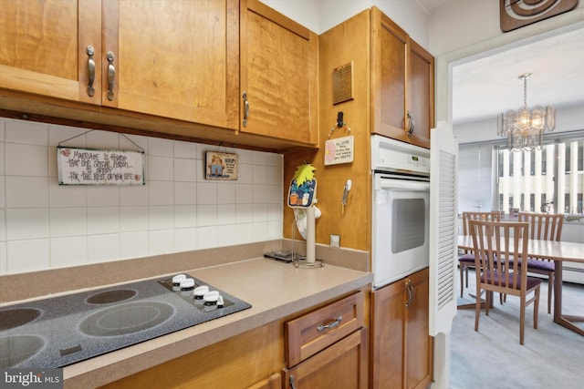 kitchen with an inviting chandelier, white oven, pendant lighting, electric cooktop, and decorative backsplash