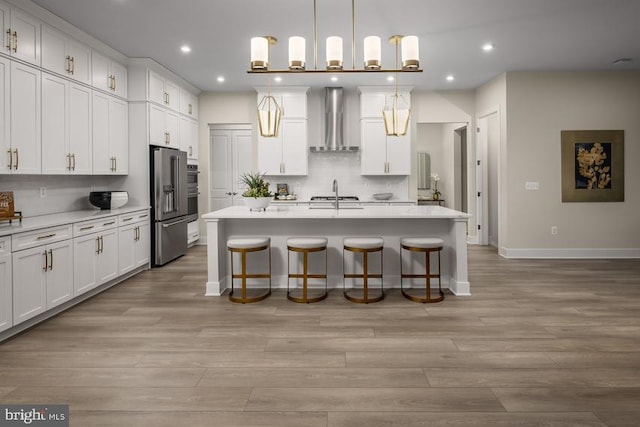 kitchen with white cabinets, wall chimney exhaust hood, decorative light fixtures, a kitchen bar, and a kitchen island with sink