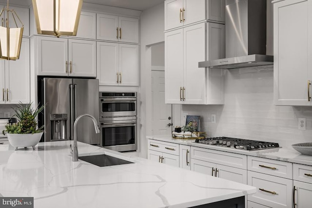 kitchen with white cabinetry, appliances with stainless steel finishes, pendant lighting, light stone countertops, and wall chimney exhaust hood