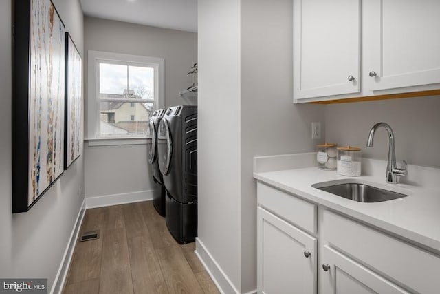 laundry area featuring light hardwood / wood-style floors, sink, washing machine and clothes dryer, and cabinets