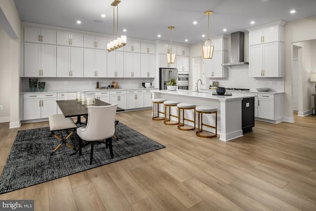 kitchen featuring white cabinetry, wall chimney exhaust hood, decorative light fixtures, and a kitchen island with sink