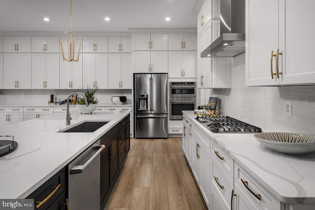 kitchen with light stone countertops, appliances with stainless steel finishes, wall chimney range hood, and pendant lighting