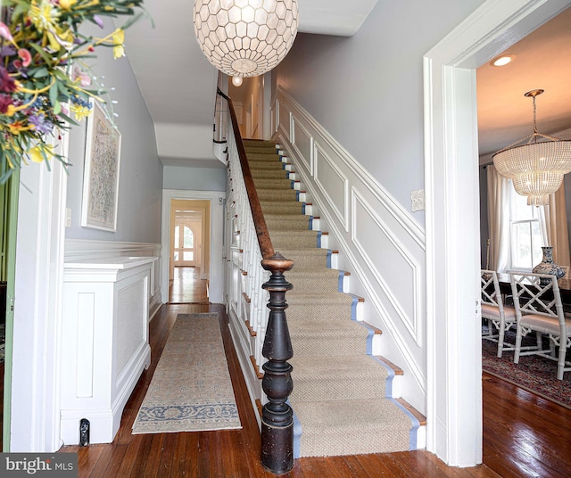 stairs with wood-type flooring and a notable chandelier