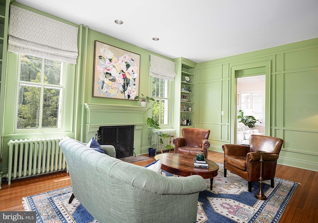 living room featuring wood-type flooring, built in features, and radiator