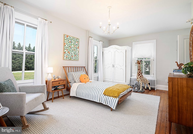 bedroom with radiator heating unit, an inviting chandelier, multiple windows, and hardwood / wood-style floors