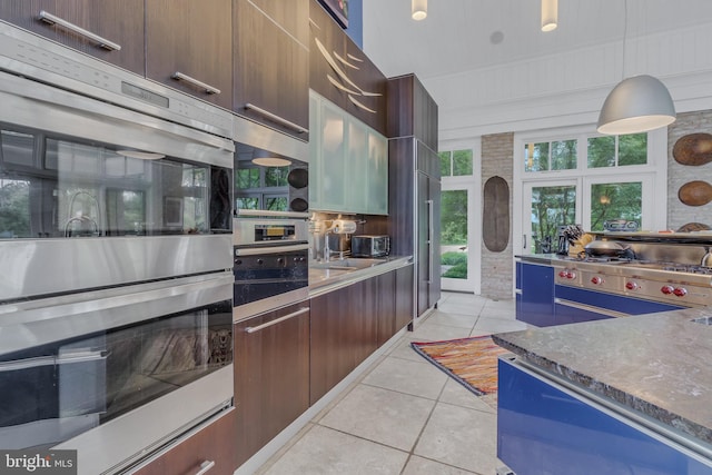 kitchen with double oven, wood walls, pendant lighting, dark brown cabinets, and light tile patterned floors