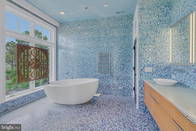 bathroom with vanity, a bath, and tile walls