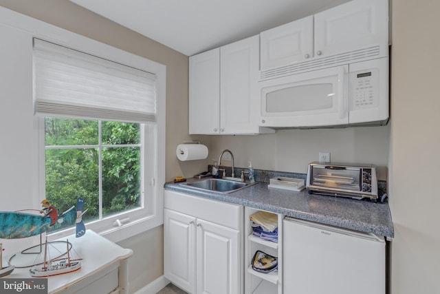 kitchen with sink, white cabinets, and fridge