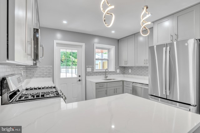 kitchen featuring sink, tasteful backsplash, light stone counters, pendant lighting, and appliances with stainless steel finishes