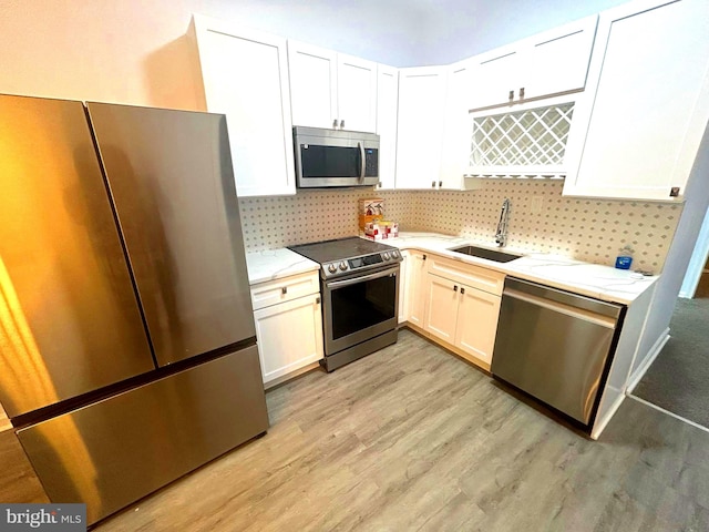 kitchen with decorative backsplash, appliances with stainless steel finishes, light wood-type flooring, sink, and white cabinetry