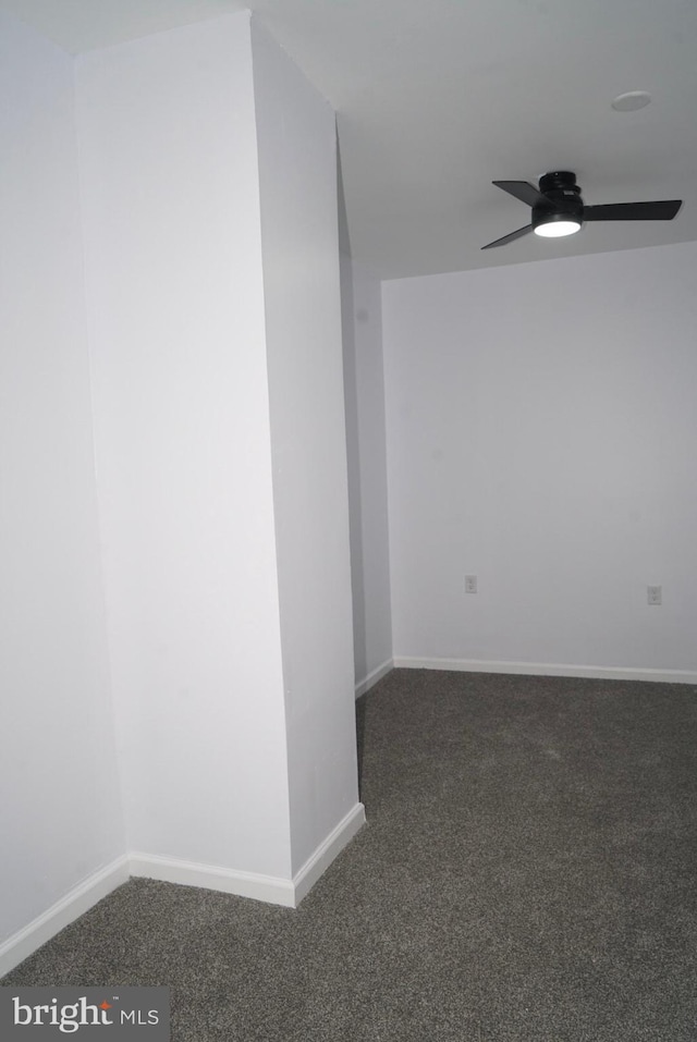 empty room featuring dark colored carpet, a ceiling fan, and baseboards