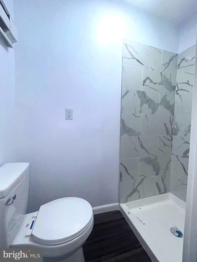 bathroom with hardwood / wood-style floors, toilet, tiled shower, and a wall unit AC