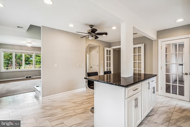 kitchen with dark stone counters, french doors, ceiling fan, a kitchen island, and white cabinetry