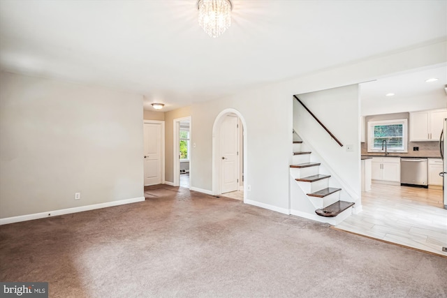 unfurnished living room featuring sink, light colored carpet, and a notable chandelier