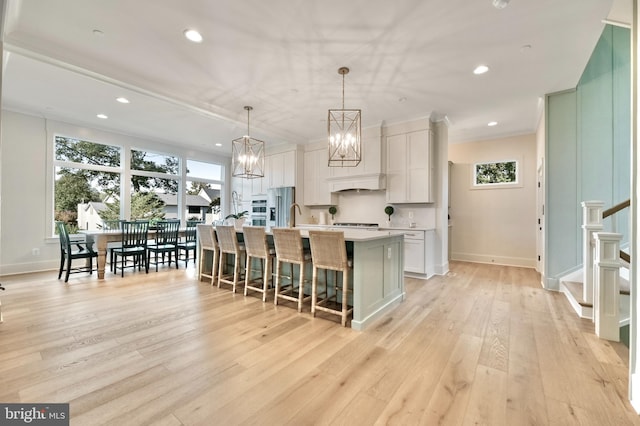 kitchen with a kitchen breakfast bar, light wood-type flooring, a kitchen island with sink, pendant lighting, and white cabinets