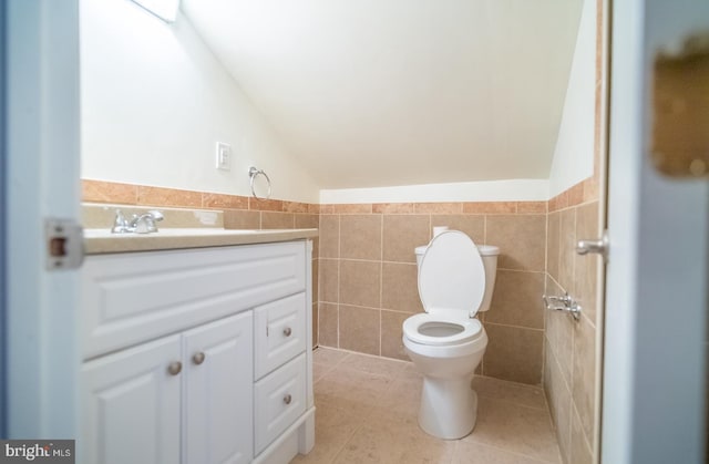 bathroom featuring tile patterned flooring, lofted ceiling, toilet, vanity, and tile walls